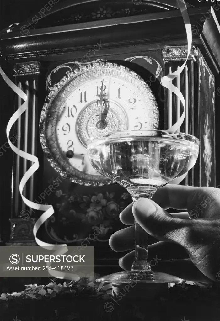 Hand holding champagne flute with champagne, clock showing 12 o'clock in the background