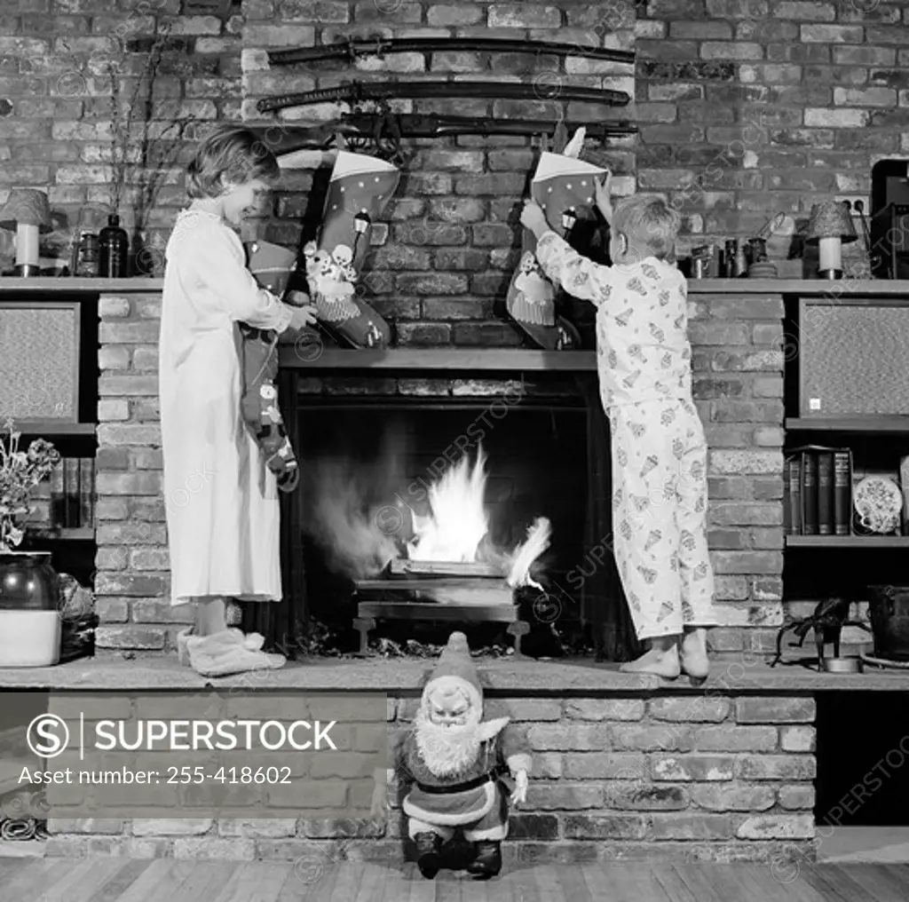 Girl and boy decorating fireplace with christmas stockings