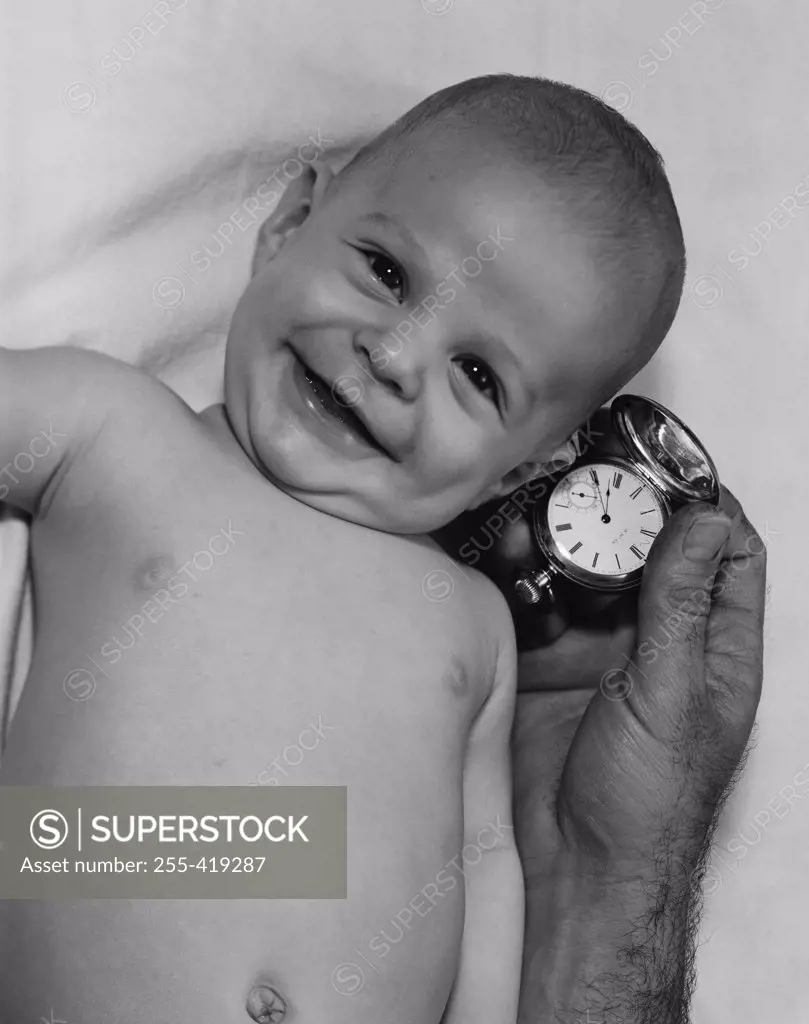 Smiling baby and hand of adult man holding watch