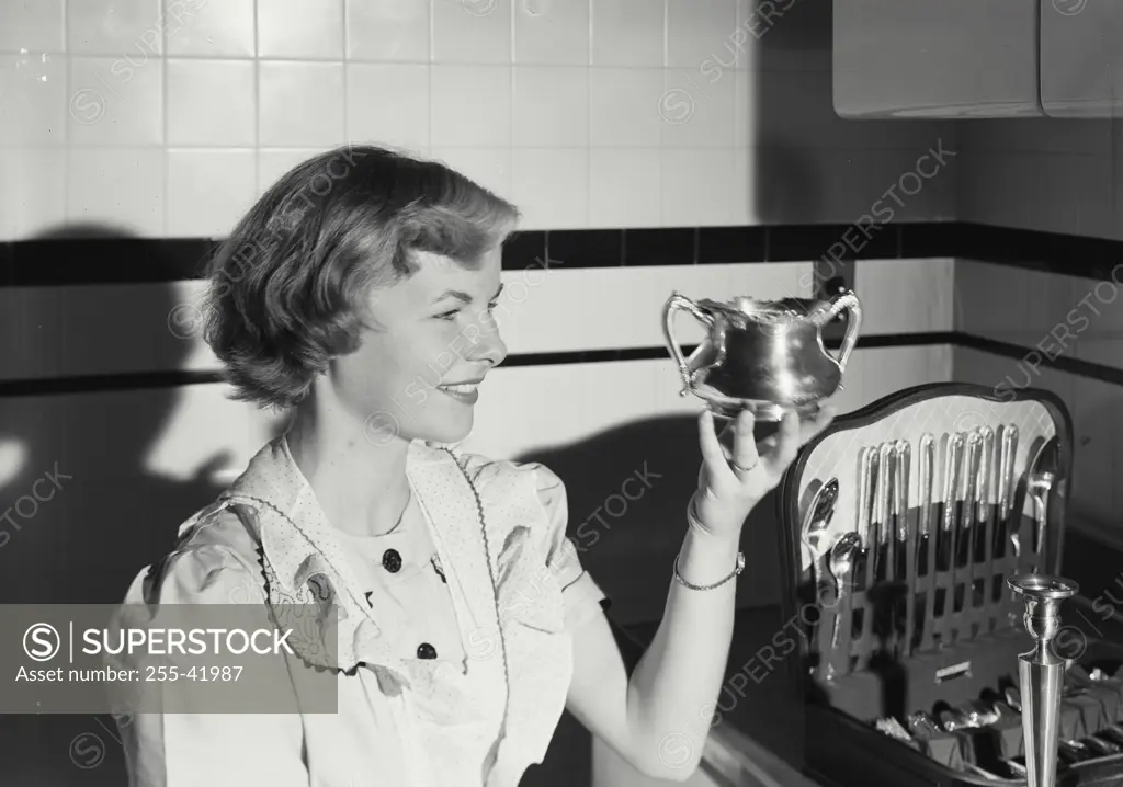 Vintage photograph. Close-up of a young woman in kitchen holding up silver bowl