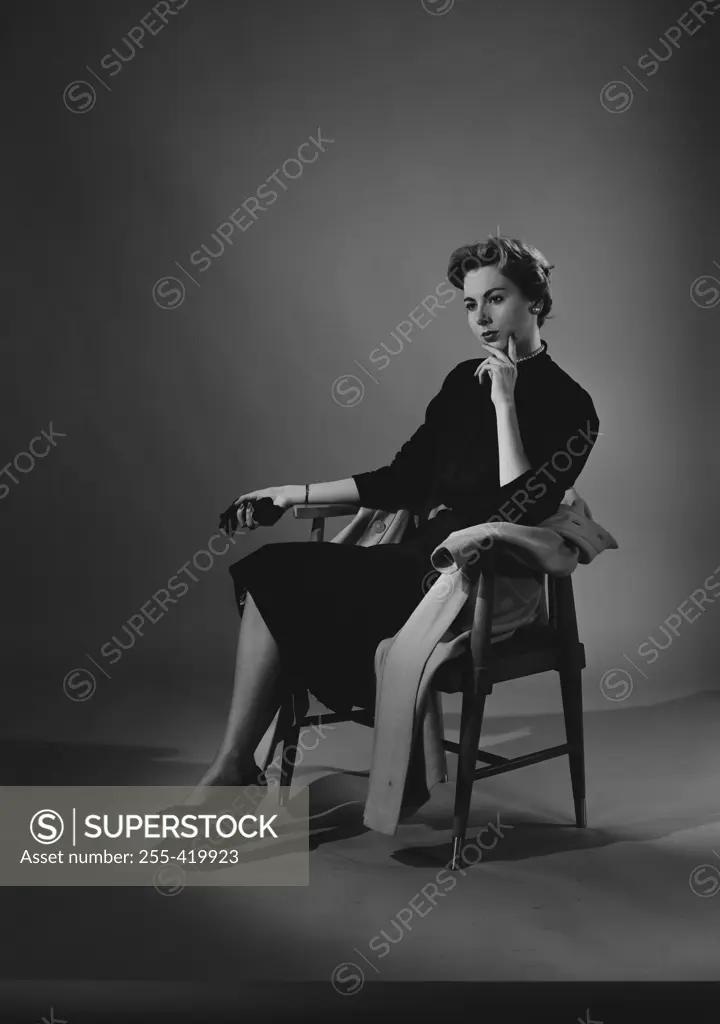 Portrait of thoughtful young woman sitting at chair, studio shot