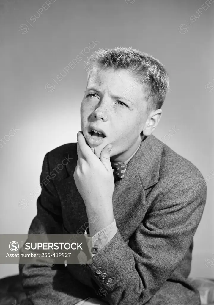 Thoughtful boy with hand on chin looking up, studio shot