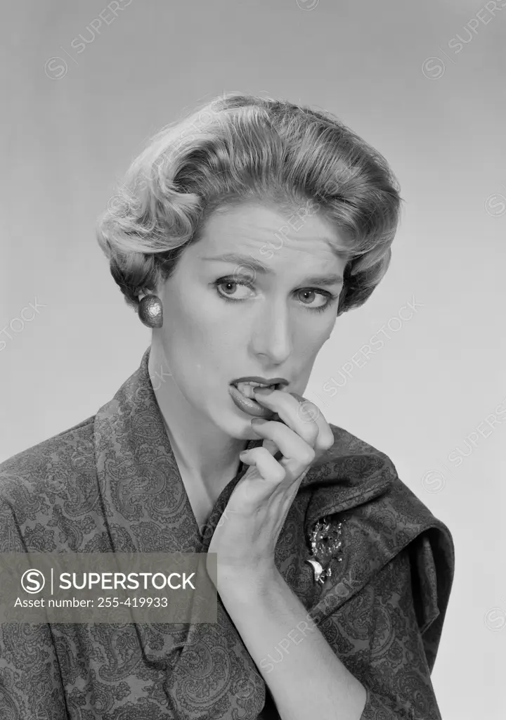 Mid adult woman biting her nails and looking away, studio shot