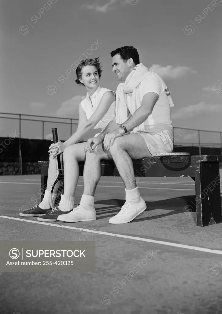 Young couple sitting by tennis court