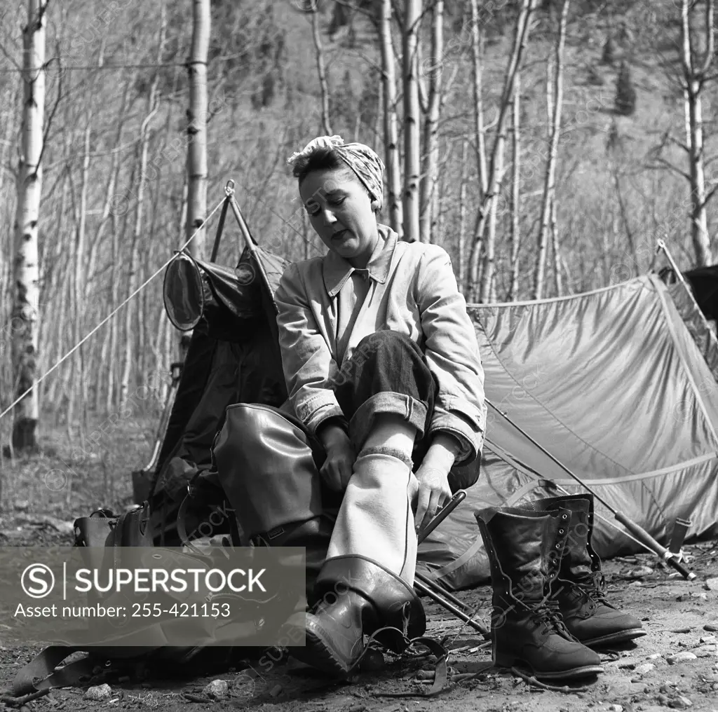 Woman putting on waders in front of tent