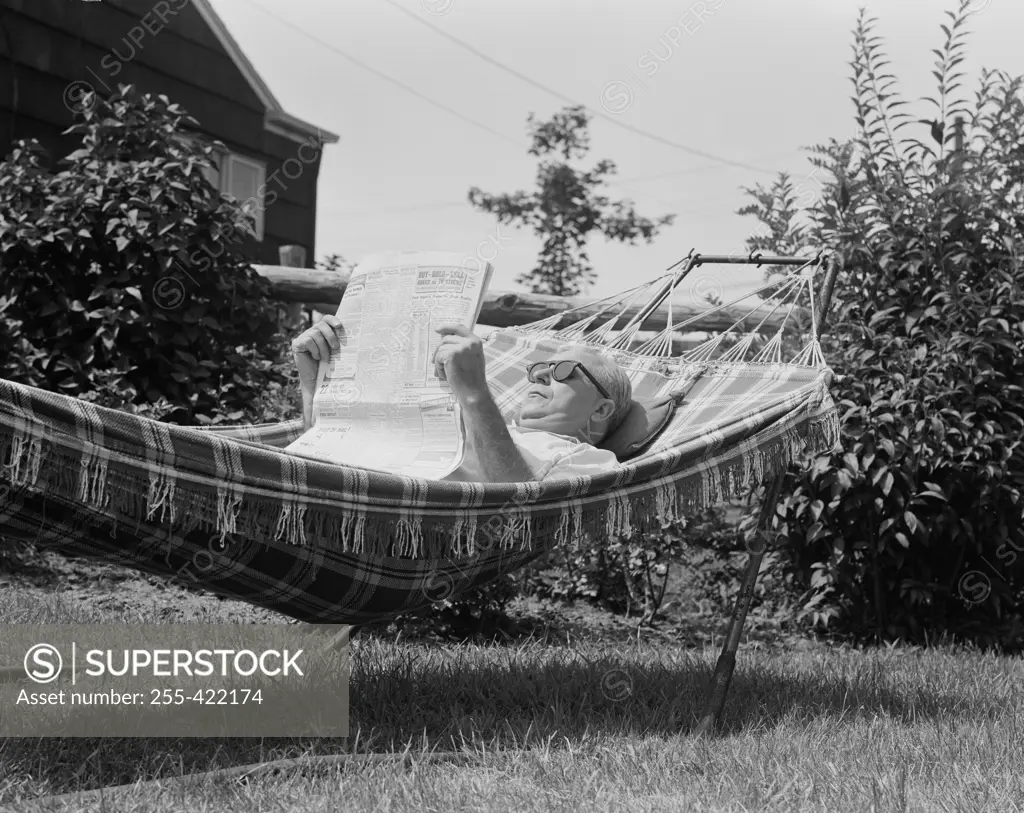 Senior man reading newspaper in hammock