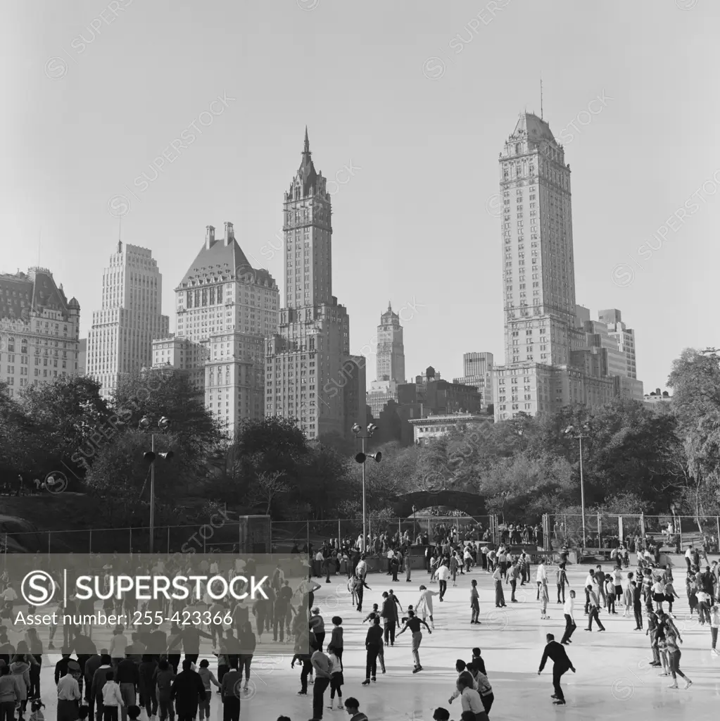 USA, New York City, Central Park, People ice-skating in front of skyline