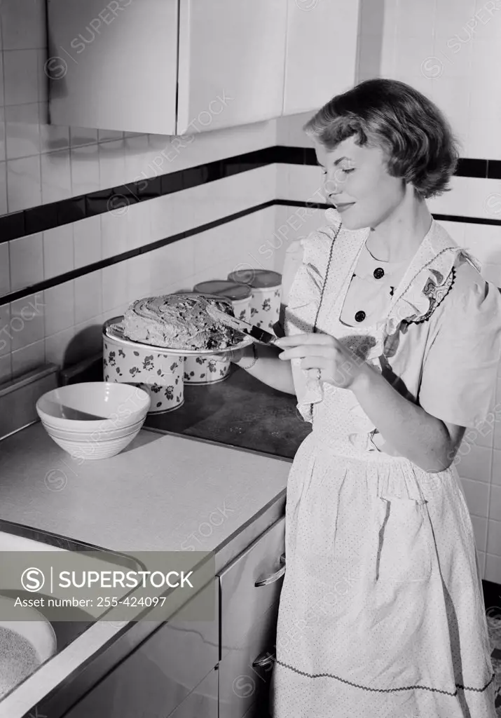 Young woman icing cake in kitchen