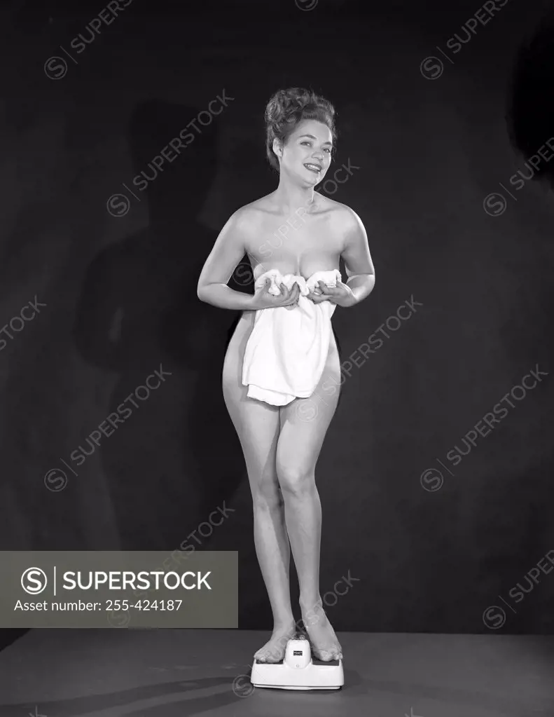 Studio portrait of naked young woman holding towel on scales - SuperStock