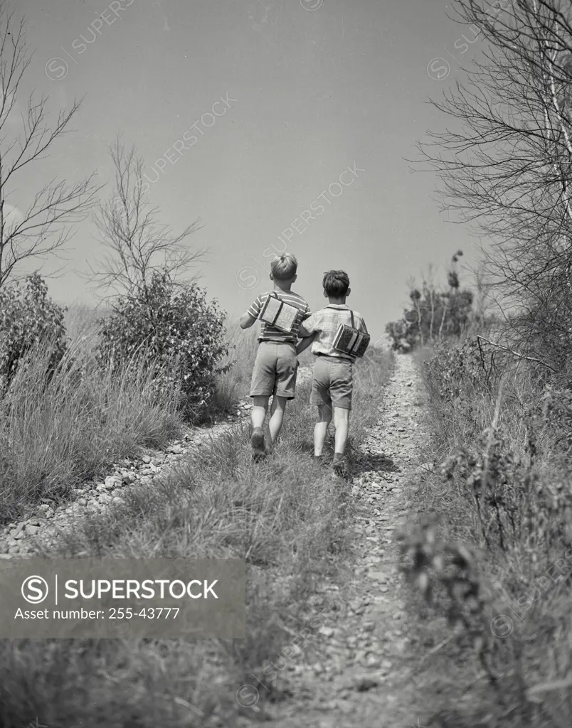 Vintage Photograph. Two young boys walking down a trail with school packs