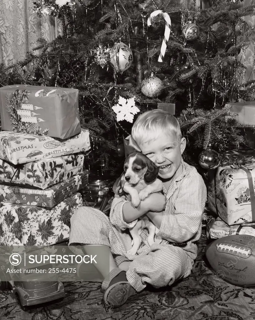 Portrait of a boy sitting near Christmas presents and hugging his puppy