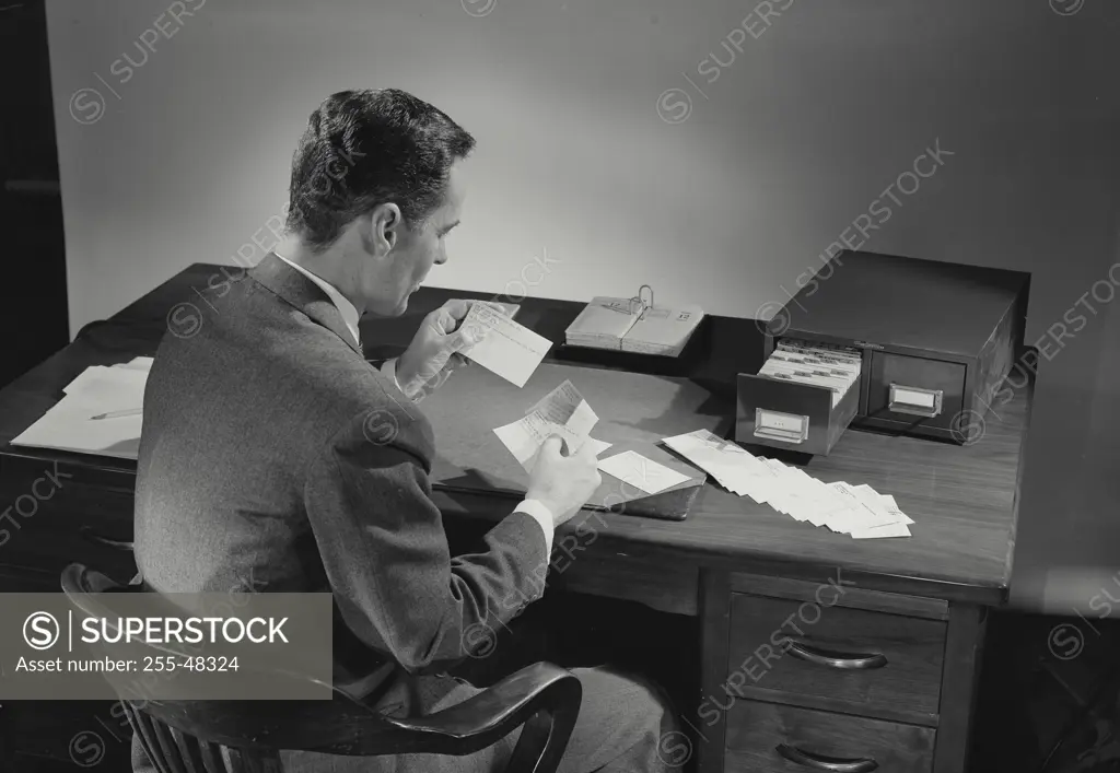 Vintage Photograph. Man in suit sitting at desk covered in papers. Frame 2