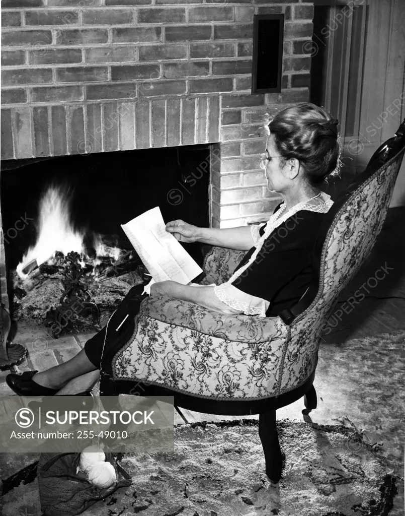 Woman reading letter by fireplace