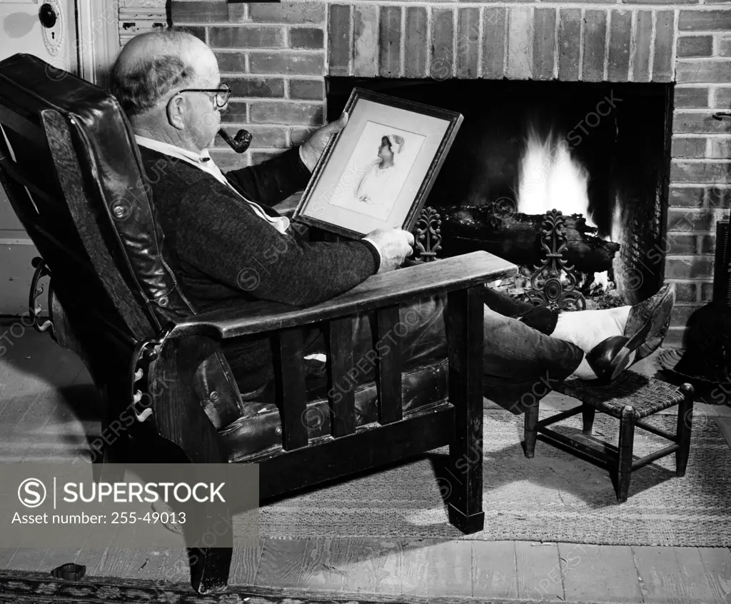 Man looking at old photograph by fireplace