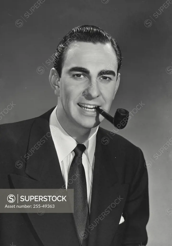 Man with black slicked back hair wearing suit and tie with wooden pipe in mouth