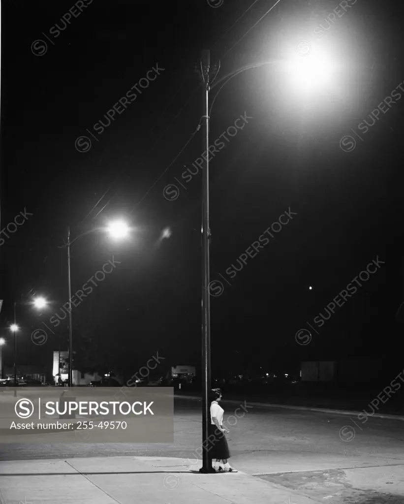 Woman leaning on lamp post in street