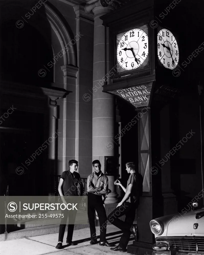 Three men having conversation outside bank at night