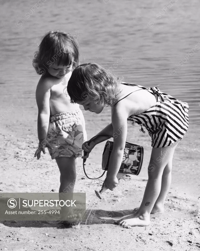 Girl pouring water on the foot of another girl on the beach