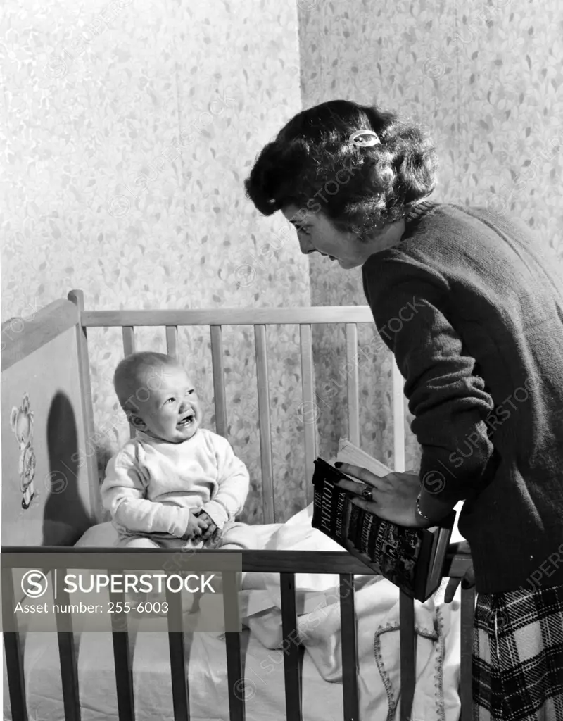 Mother standing at crying baby boy sitting in crib