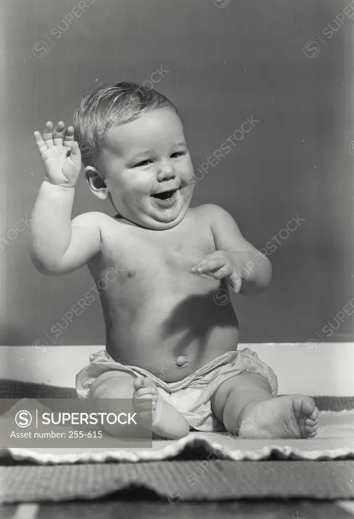 Vintage Photograph. Smiling baby sitting on towel with arms raised