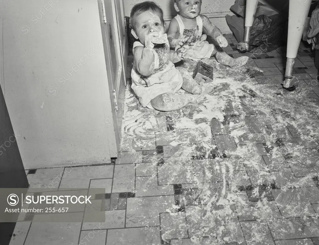 Vintage Photograph. Babies playing in a mess made of flour on kitchen floor