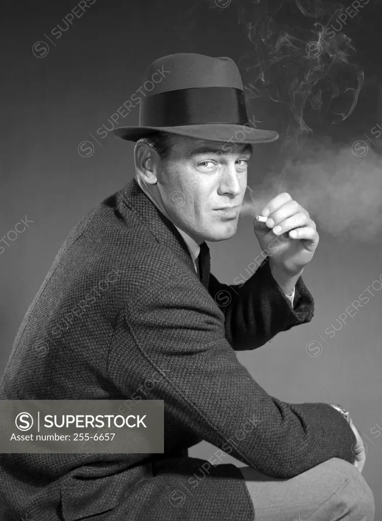 Studio portrait of man wearing hat, smoking cigarette