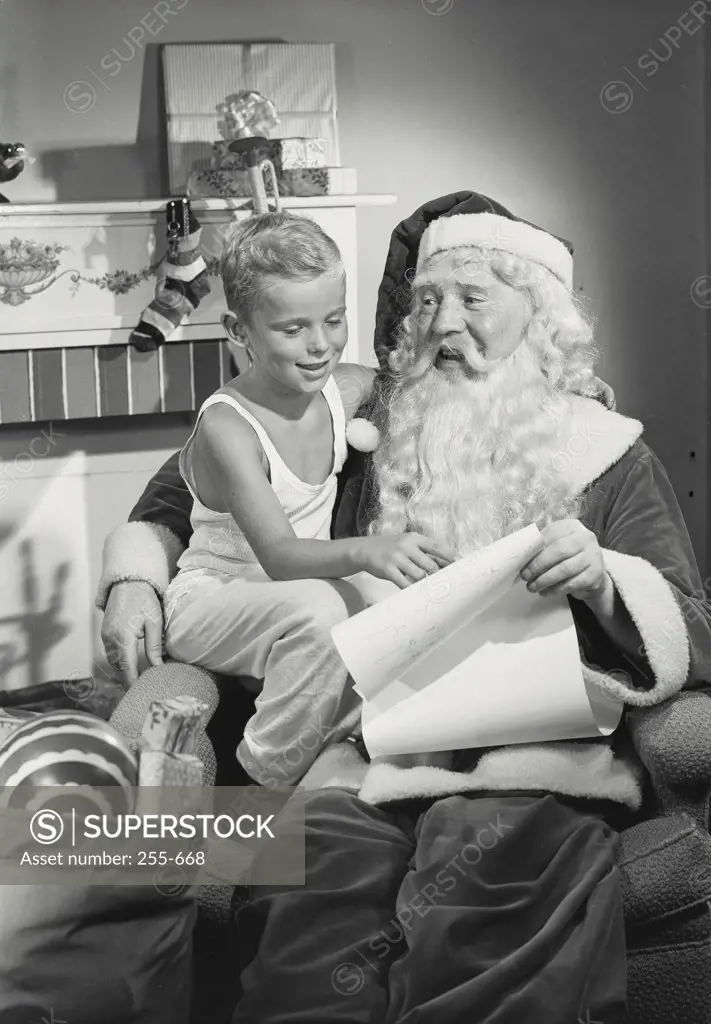 Vintage photograph. Young boy sitting with Santa Claus on chair in front of fireplace