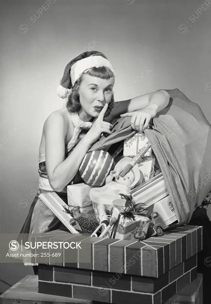 Vintage photograph. Portrait of a young woman dressed as santa quietly dumping toys down chimney