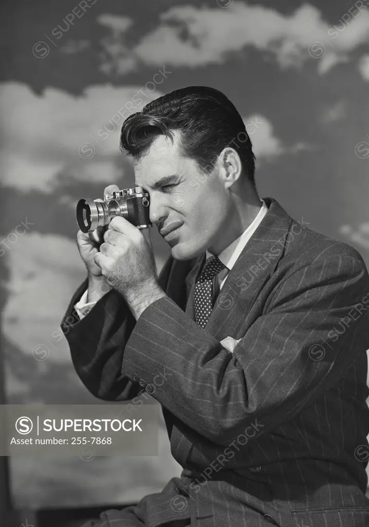 Vintage Photograph. Man looking through camera in front of cloud sky background