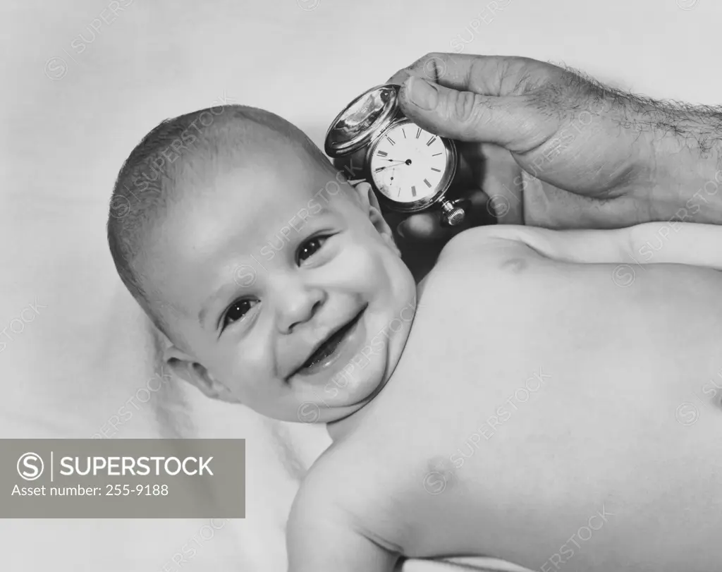 High angle view of a baby smiling and it's father holding a pocket watch near it's ear