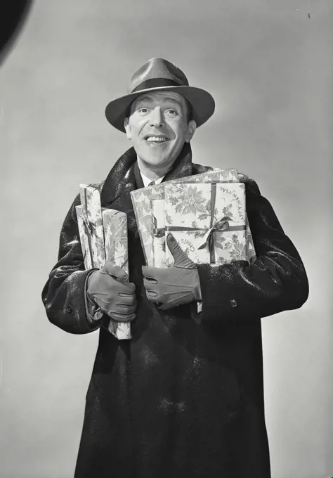 Vintage Photograph. Smiling man wearing hat and winter coat dusted with snow holding wrapped holiday presents