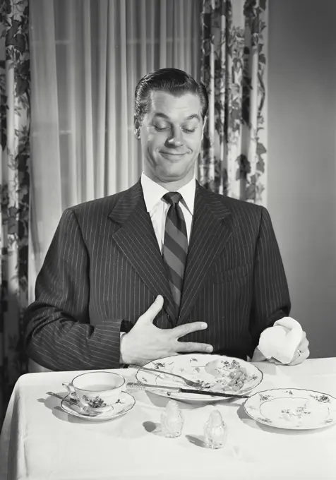 Vintage photograph. Man at table holding full stomach with empty plates