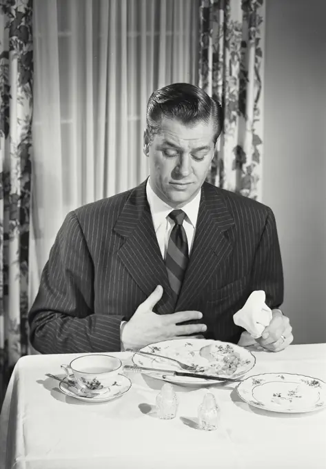 Vintage photograph. Man at table holding full stomach with empty plates