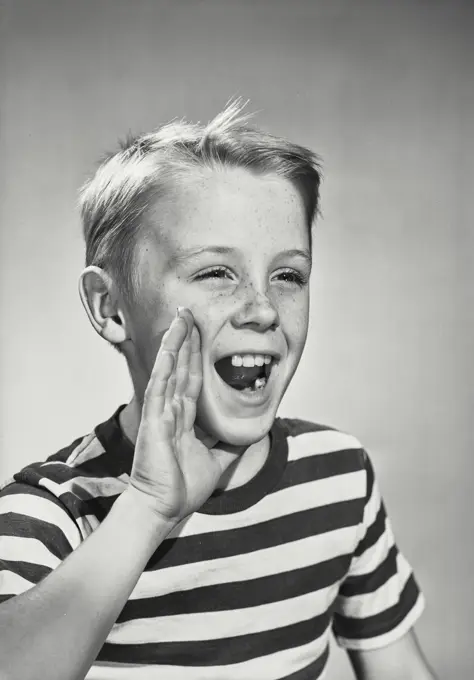 Vintage photograph. Portrait of smiling young boy wearing striped T-shirt holding up hand to mouth calling out