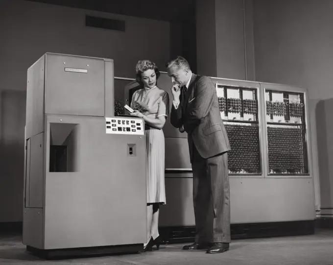 Side profile of businessman and his secretary working on computer, Univac 120