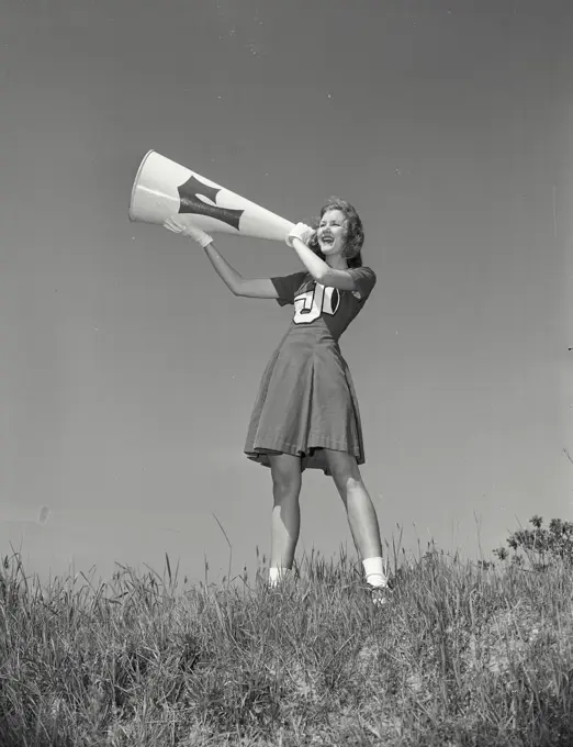 Vintage photograph. Low angle view of a female cheerleader shouting into a megaphone