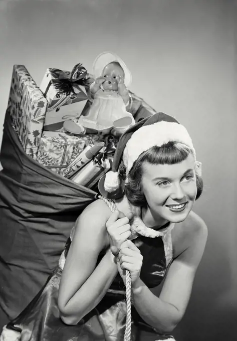 Vintage photograph. Close-up of a young woman dressed as santa with toy sack over shoulder