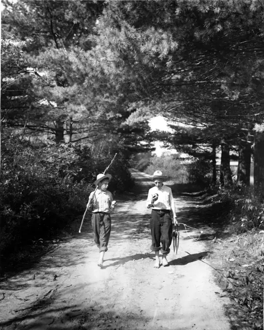 Vintage photograph of boys on forest footpath carrying improvised fishing rod and catch of fish