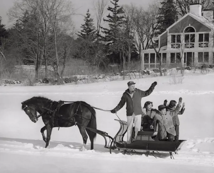 Mature couple with their children riding in a horsedrawn sleigh and waving their hands