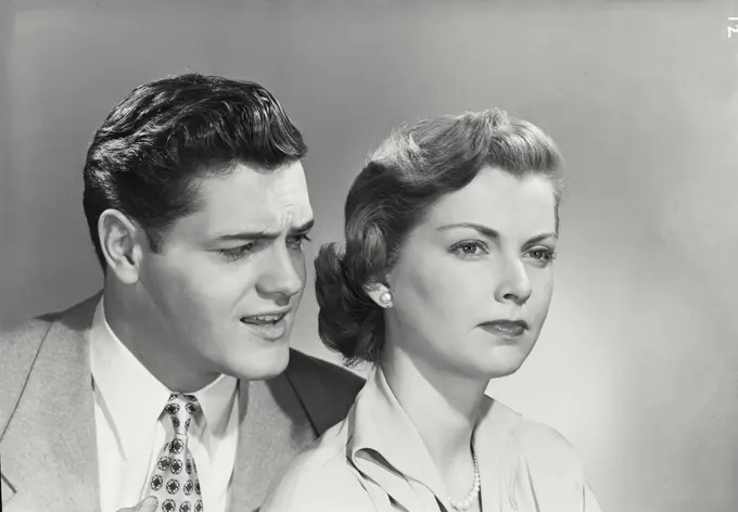 Vintage photograph. Portrait of young couple, man looking at woman who has stern expression.