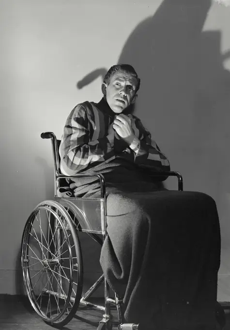 Vintage photograph. Man sitting in wheelchair clutching collar with frightened expression.