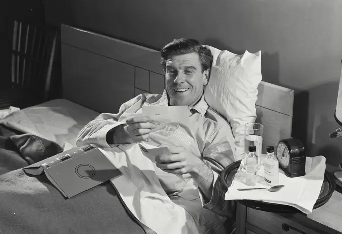 Vintage Photograph. Sick man in pajamas sitting up and reading. Frame 1