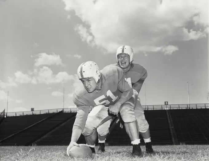 Vintage photograph. Football players - Quarterback about to recieve ball from Center. Models released 