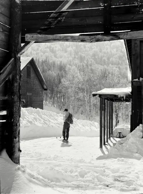 Vintage photograph. Shanty vista. View through mountain shanty house looking at man on skis in the snow