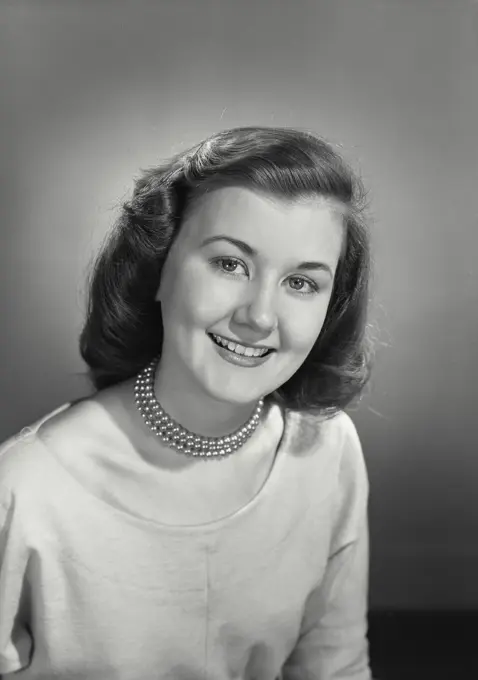 Vintage photograph. Young woman in pearl necklace smiling looking at camera