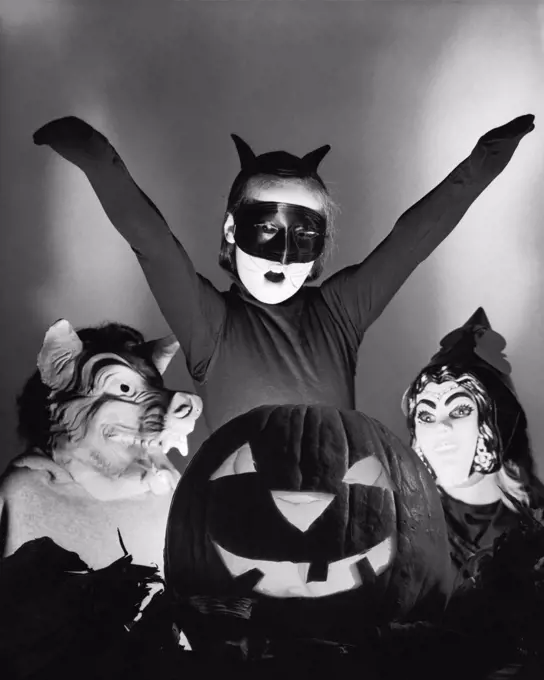 Close-up of an illuminated jack o' lantern with three people wearing Halloween costumes behind it