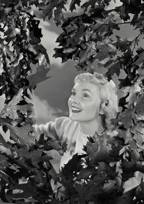 Vintage photograph. Close-up of a young woman smiling looking through branches.