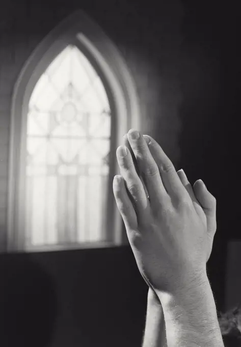 Vintage photograph. Hands clasped in prayer in front of church window