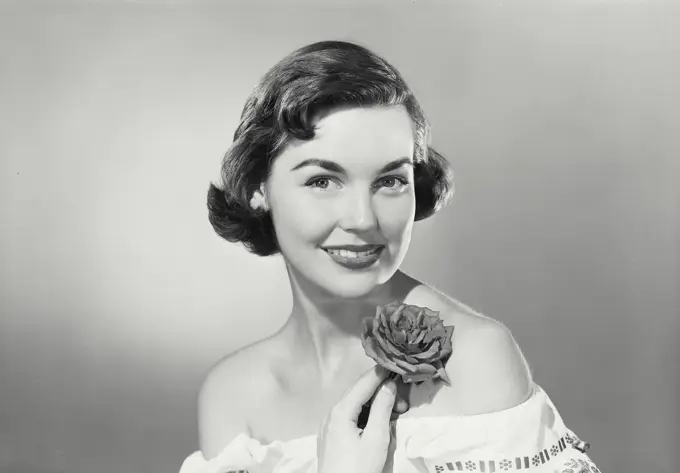 Vintage photograph. Brunette woman smiling wearing traditional Mexican dress holding rose underneath chin