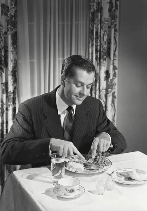 Vintage photograph. Man at table cutting food on plate.